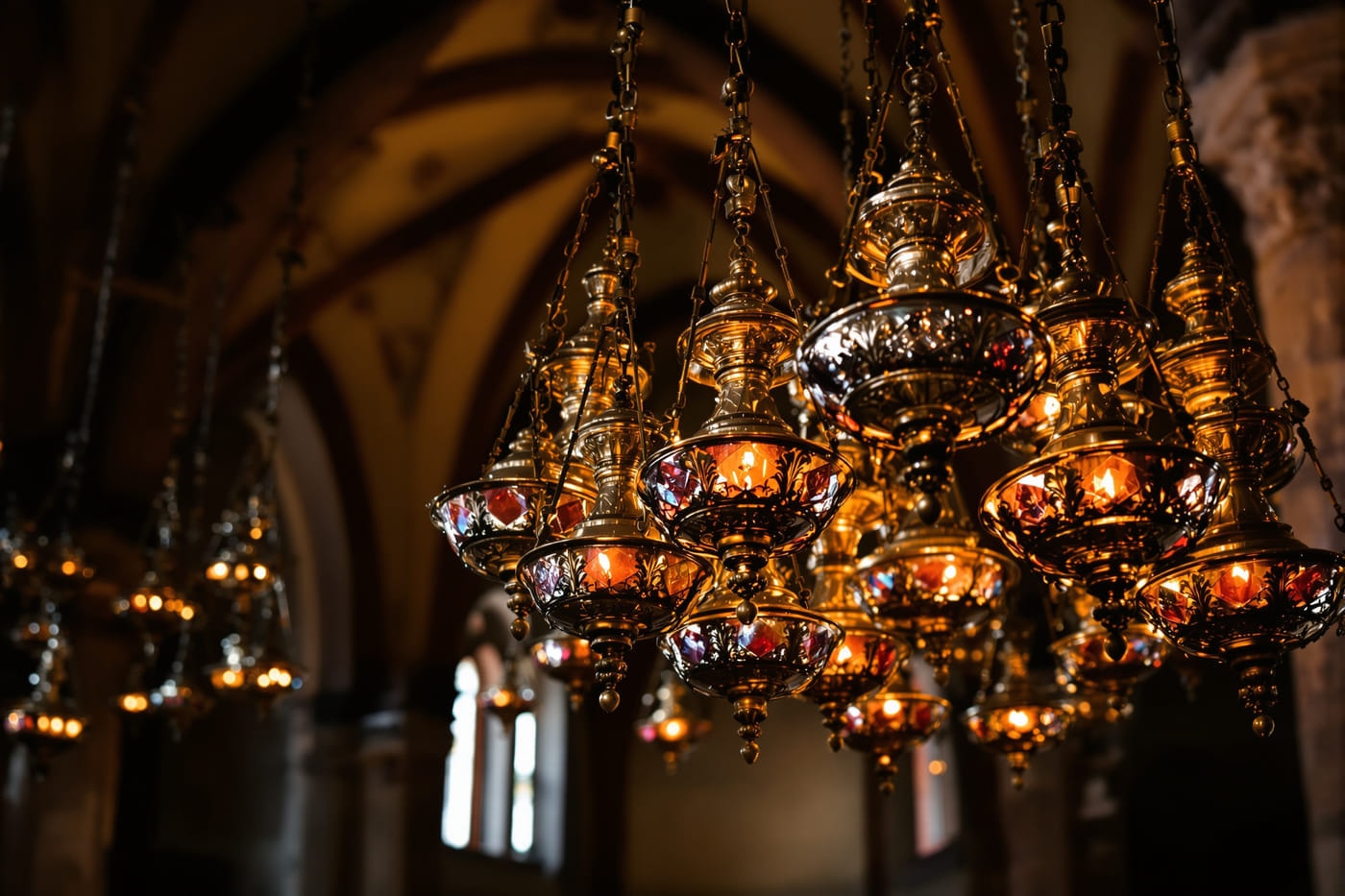 Hanging silver and brass oil lamps with small flames in a darkened stone church